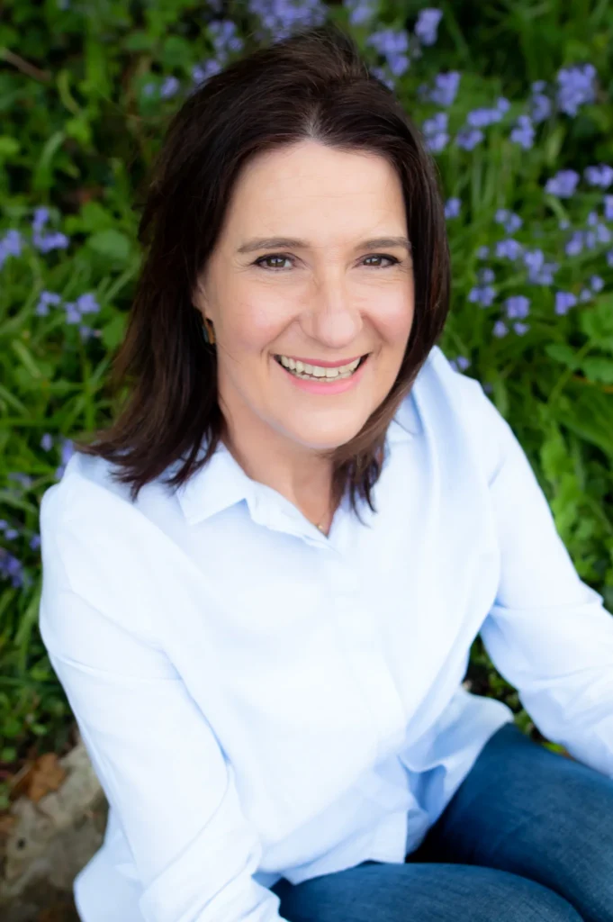 A woman wearing a light blue shirt seated outdoors surrounded by vibrant purple flowers, showcasing tranquil nature in County Wicklow.