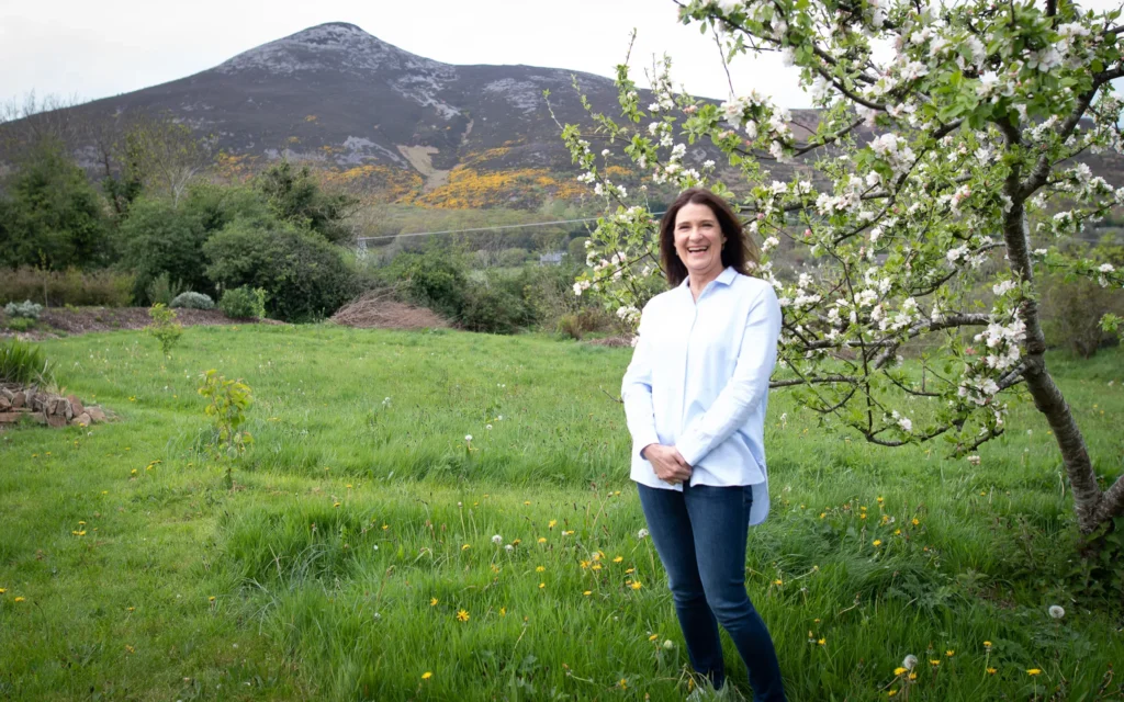 A woman wearing a light blue shirt seated outdoors surrounded by vibrant purple flowers, showcasing tranquil nature in County Wicklow.